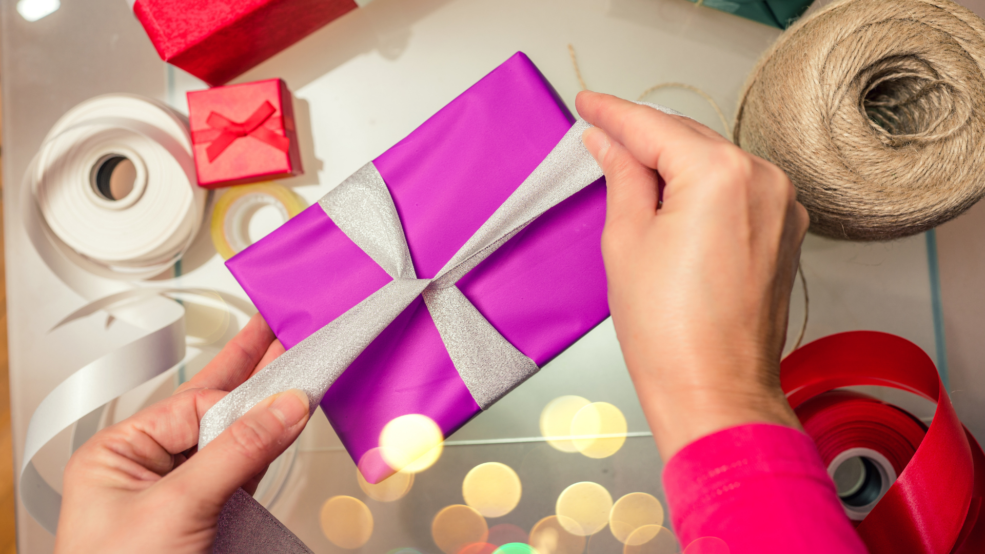 hands tying silver ribbon on gift wrapped purple box